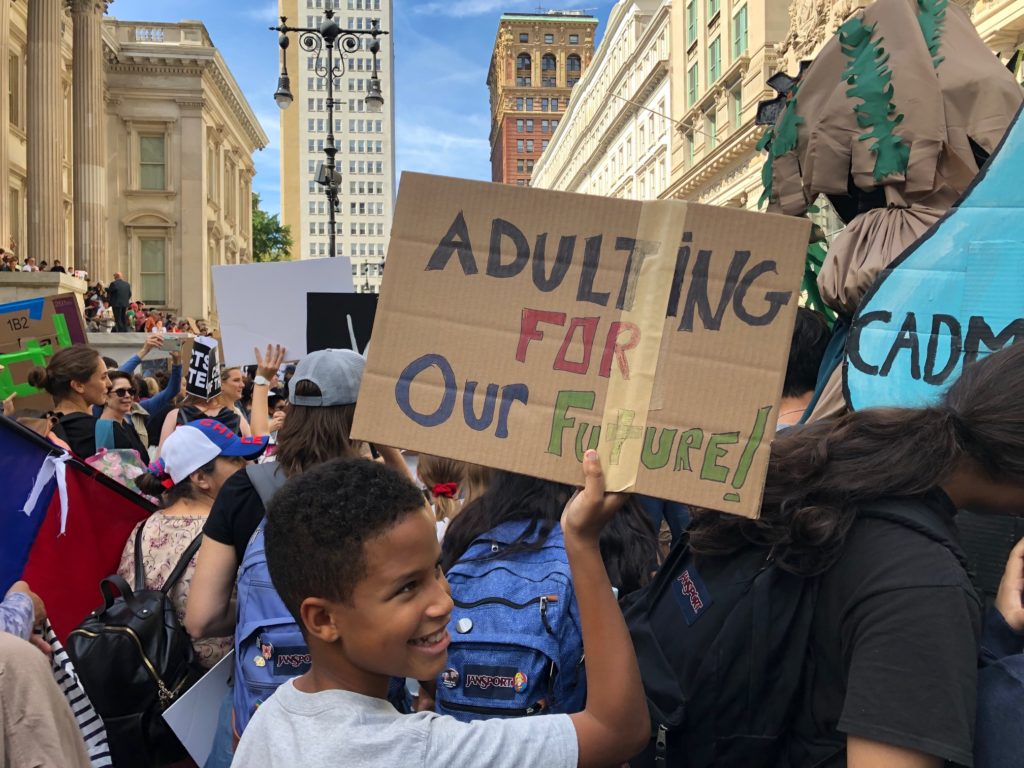 Boy holding sign with "Adulting for Our Future"