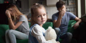 A man and a woman are in conflict while their daughter is between them looking directly at the camera.