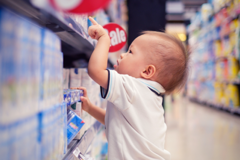 A toddler in a super market aisle points at a package.