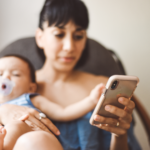 Mother with baby on her lap looking at her phone.