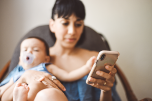 Mother with baby on her lap looking at her phone.