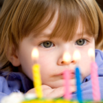 Child looking at the candles on their birthday cake.