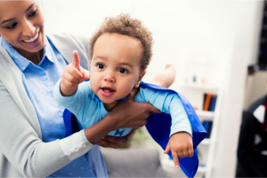 Mom holding baby in superhero costume.