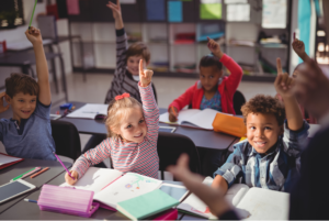 Kids in a classroom raising their hands.