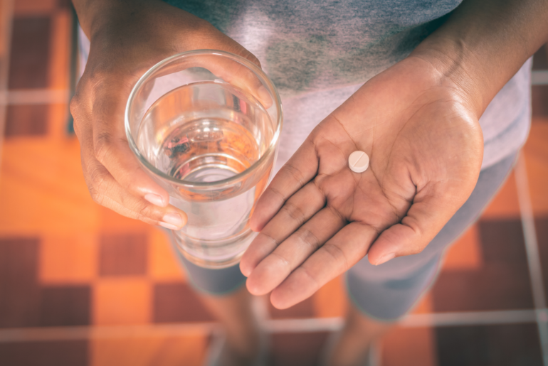 Female holding medicine pill and a glass a water.