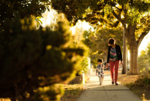 Mother walking her child on a sidewalk in late afternoon sun.