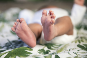 Close up on baby feet on blanket with green leaves.