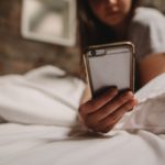 Child on bed with smartphone in foreground.