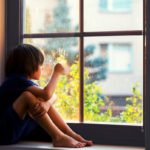 Lonely boy sitting in window sill.