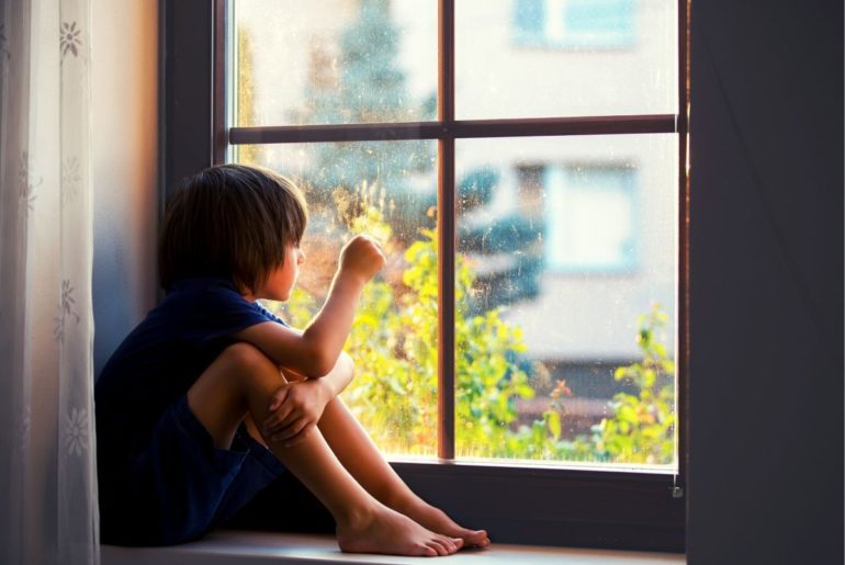 Lonely boy sitting in window sill.