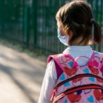 Little girl wearing facemask and a backpack to school.