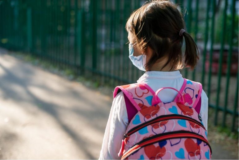 Little girl wearing facemask and a backpack to school.