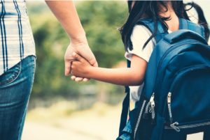 Child wearing backpack holds parent's hand.