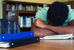 Frustrated student without laptop with his head in his arms.