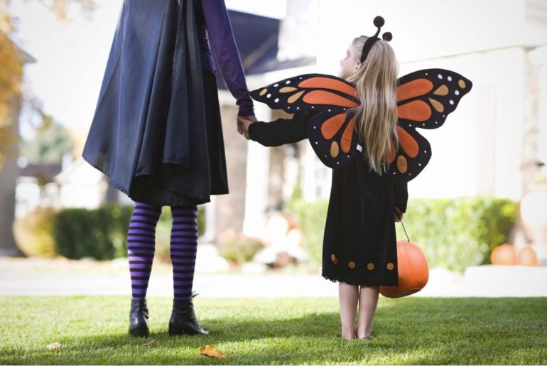 Girl in butterfly costume holding mom's hand.