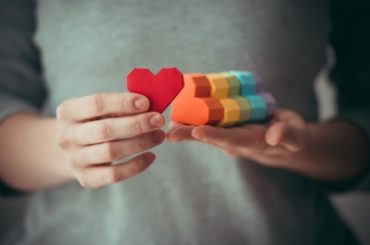 A person holding a set of multi colored wooden hearts to symbol creating welcoming spaces for LGBTQ+ kids.