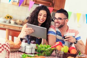 Couple enjoying dinner while looking at a tablet.