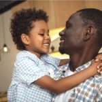 Father and child smiling at each other and hugging.