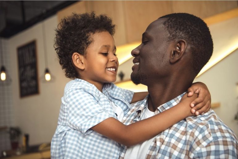 Father and child smiling at each other and hugging.