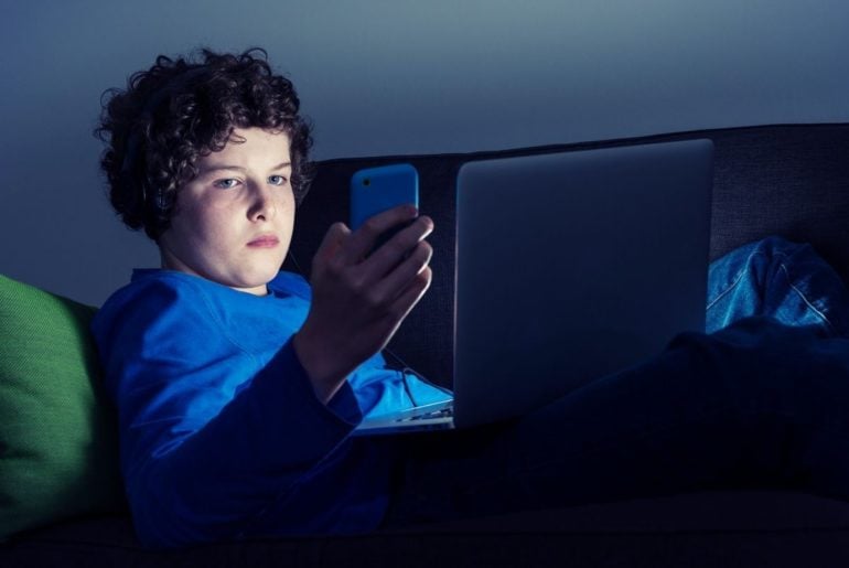 Teen boy on couch with laptop and smarthphone.