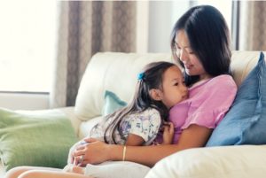 Mother and daughter hugging and talking on couch.