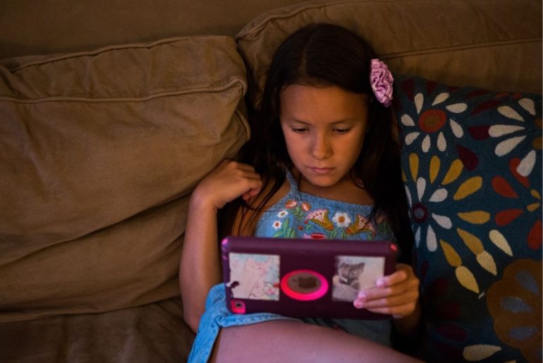 Tween girl on couch looking at tablet.