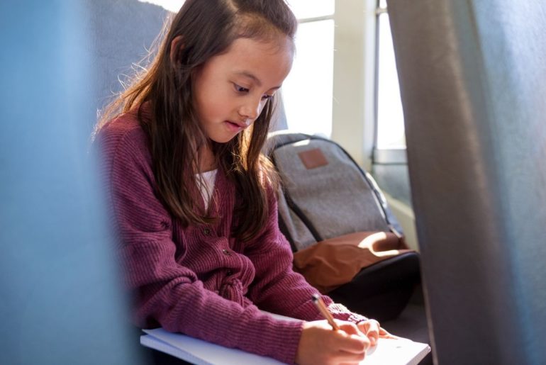 Girl on bus doing schoolwork.