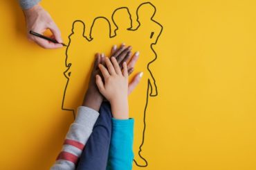 Foster family with hands overlapping on outline of a family drawing.
