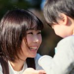 Mother kneeling down and smiling at toddler.