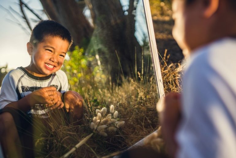 Boy looking in a mirror outdoors.