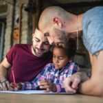 Same sex couple helping adopted daughter with homework.