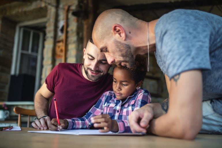 Same sex couple helping adopted daughter with homework.