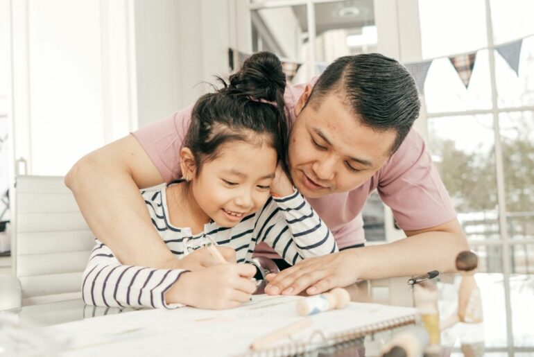 Father helping child at kitchen table.