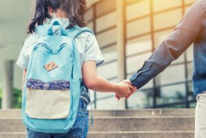 Girl wearing backpack on school steps holding parent's hand.