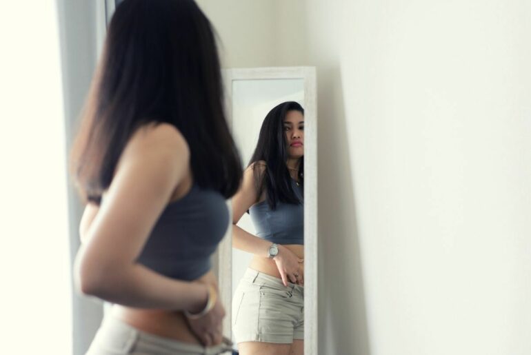 Young woman unhappy with her reflection in mirror.