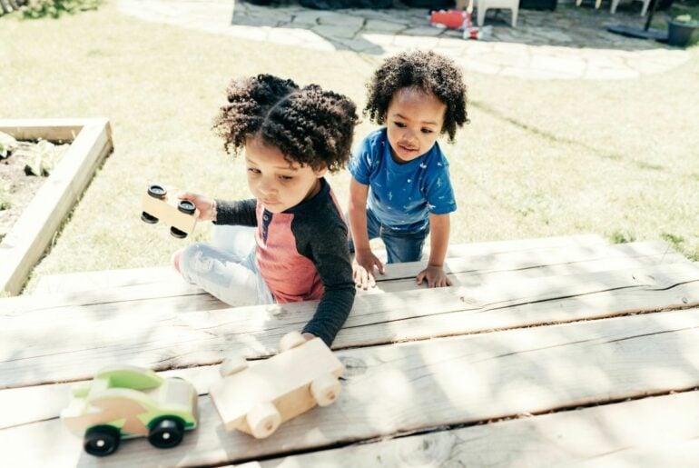 Two young kids playing with toy cars outside.