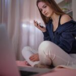 Worried teen girl sitting on bed looking at laptop.