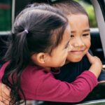 Siblings hugging and smiling in car window.