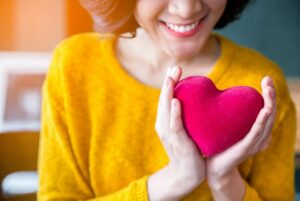 Smiling woman feeling grateful holding a heart near her chest.