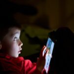 Boy looks scared using tablet in the dark.