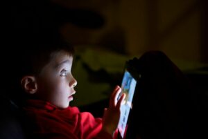 Boy looks scared using tablet in the dark.