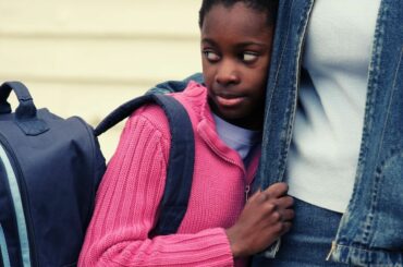 Shy girl who needs to learn self-advocacy skills holding onto parent's waist