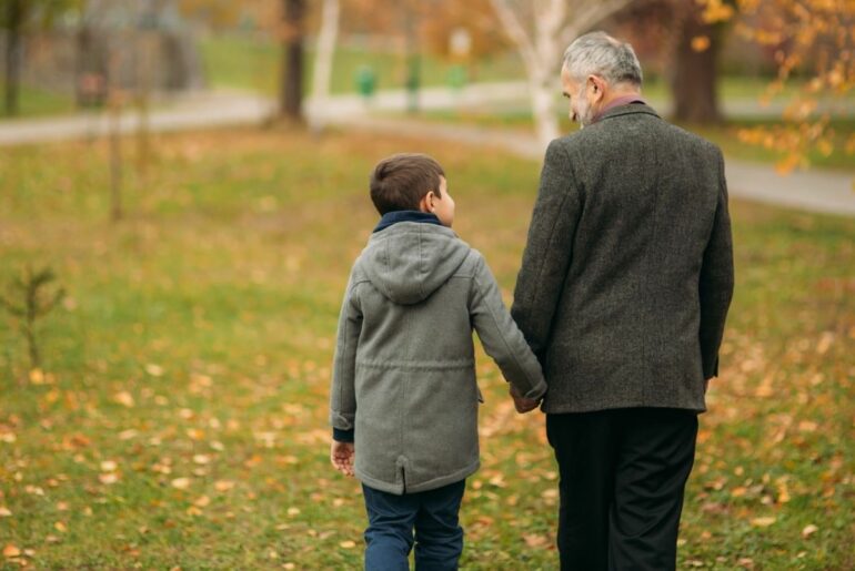 Grandfather and grandson holding hands as they walk in a park.