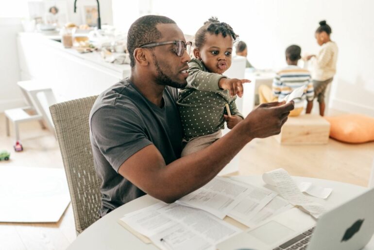 Father holding toddler while completing family taxes.