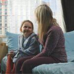 Mom talking to preteen daughter on her bed.