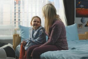 Mom talking to preteen daughter on her bed.