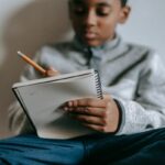 Focused boy sitting cross legged and writing in notebook.