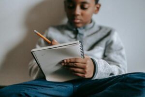 Focused boy sitting cross legged and writing in notebook.