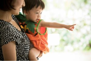 Mother holding baby who is pointing at something out the window.