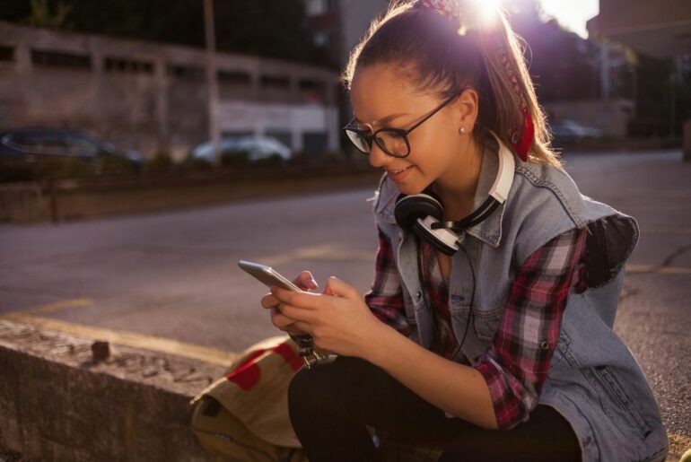 Teen sitting outside school and smiling at her phone.